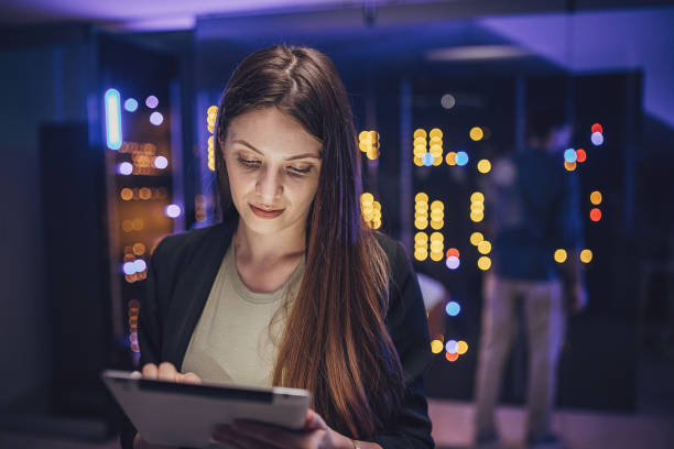 female maintenance engineer examining data on digital tablet in server room.